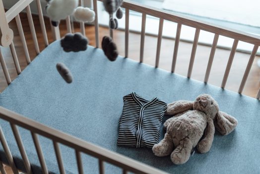 Baby clothing and a bunny soft toy laying on a baby cot bed. Preparing for new born baby.