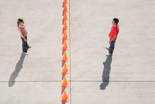 Man and woman on either side of row of traffic cones looking back Man and woman on either side of row of traffic cones looking back