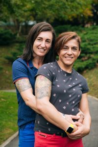 Portrait of a happy middle aged lesbian couple hugging and looking to camera in a park