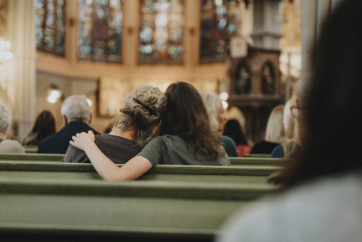Teenage daughter sitting with arm around mother on bench at protestant church