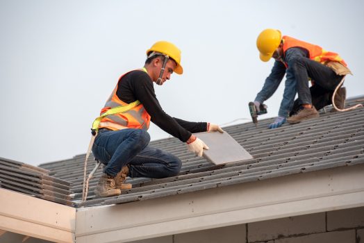 working on the roof structure of the building on the construction site, Roofer Construction worker wearing safety belt while working on the roof structure of the building on the construction site, Roofer uses a drill and installs concrete roof tiles on the roof.