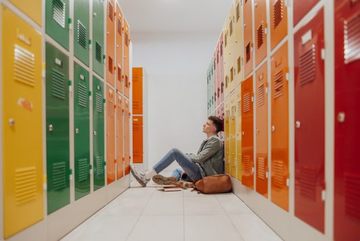Sad pensive teenager sitting alone in the floor in locker room.