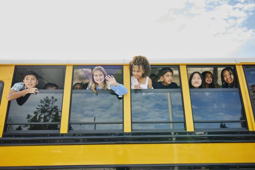 Medium wide shot middle school kids looking out windows of school bus Medium wide shot of smiling middle school kids looking out open windows of school bus
