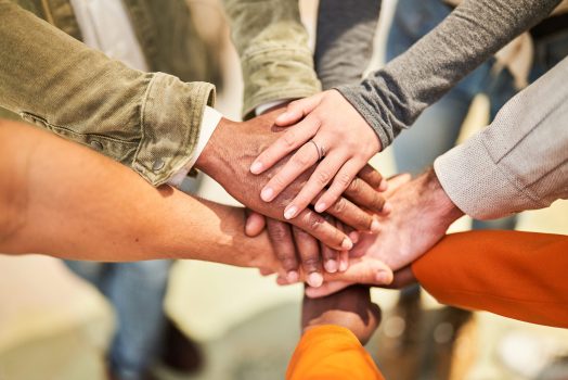 Cropped shot of multi-ethnic group of business people with stacked hands showing unity and teamwork. Unrecognizable business people stacking hands in modern office