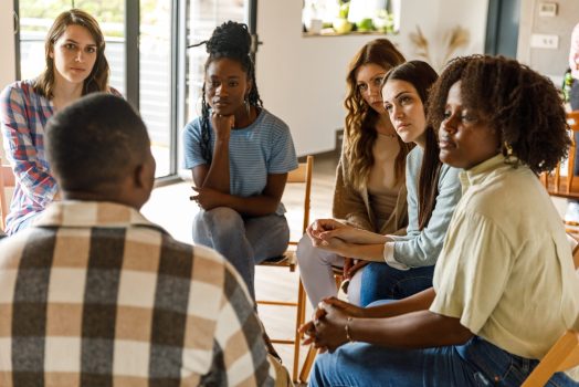 Compassionate group of people listening to young man sharing his problems during a group therapy session Selective focus shot of diverse group of young people sitting in a circle and listening, with compassion, to a young man sharing his problems during a group therapy session.