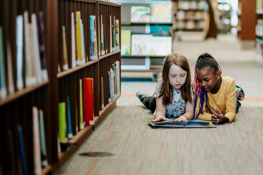 Two young girls reading a book on the floor of library